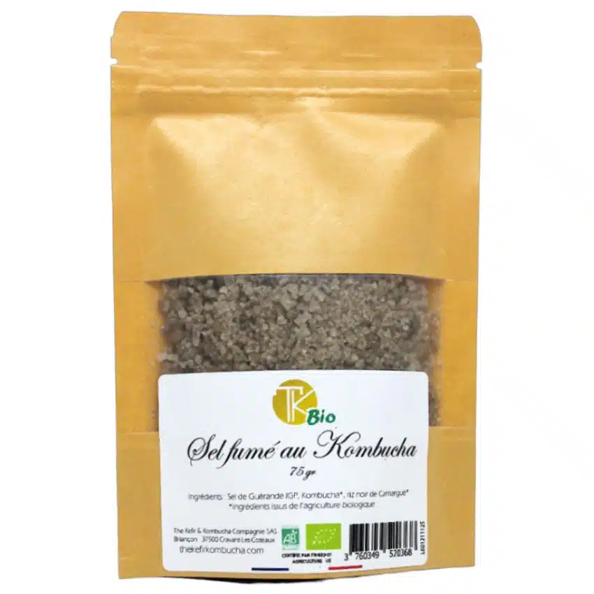 image d'un sachet marron de sel infusé au kombucha avec un rectangle transparent laissant apparaitre le produit. L'étiquette centrale est rectangulaire et comporte le nom du produit, le logo et les informations importantes